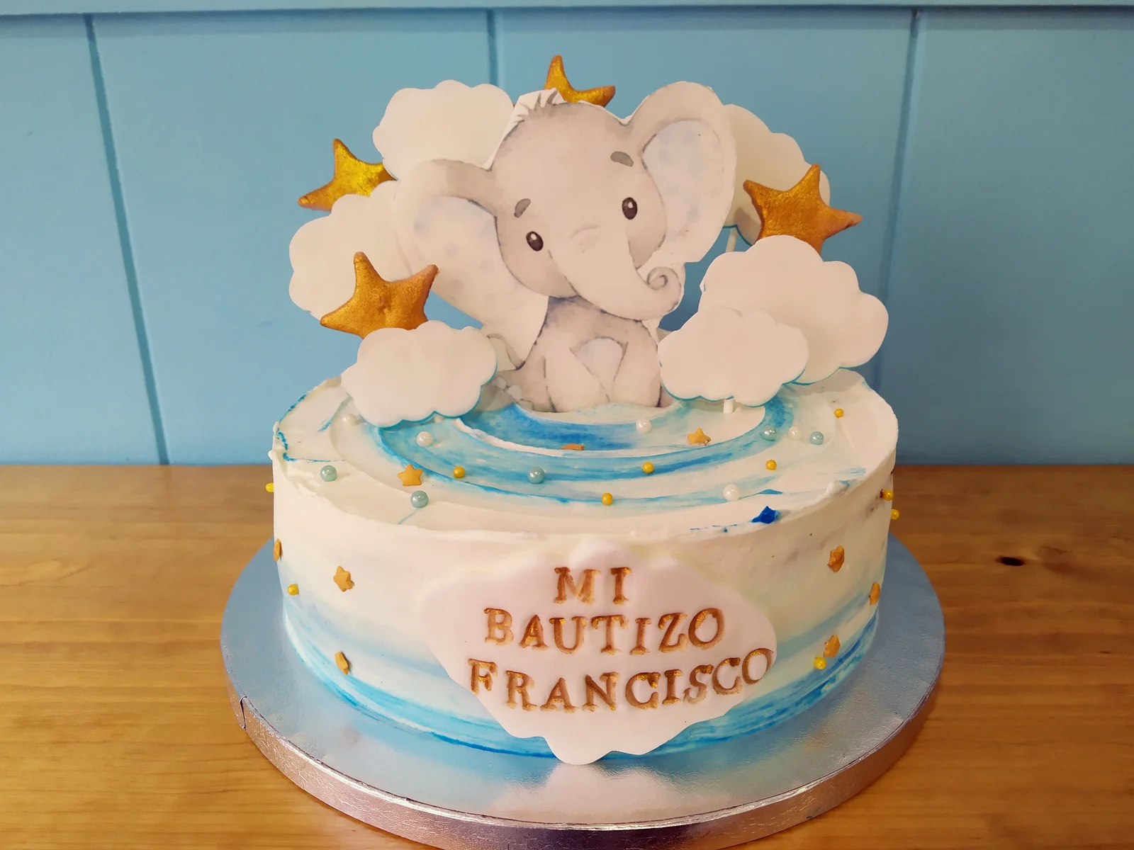 Tarta de bautizo con elefante de fondant sobre nubes, estrellas doradas y el nombre Francisco