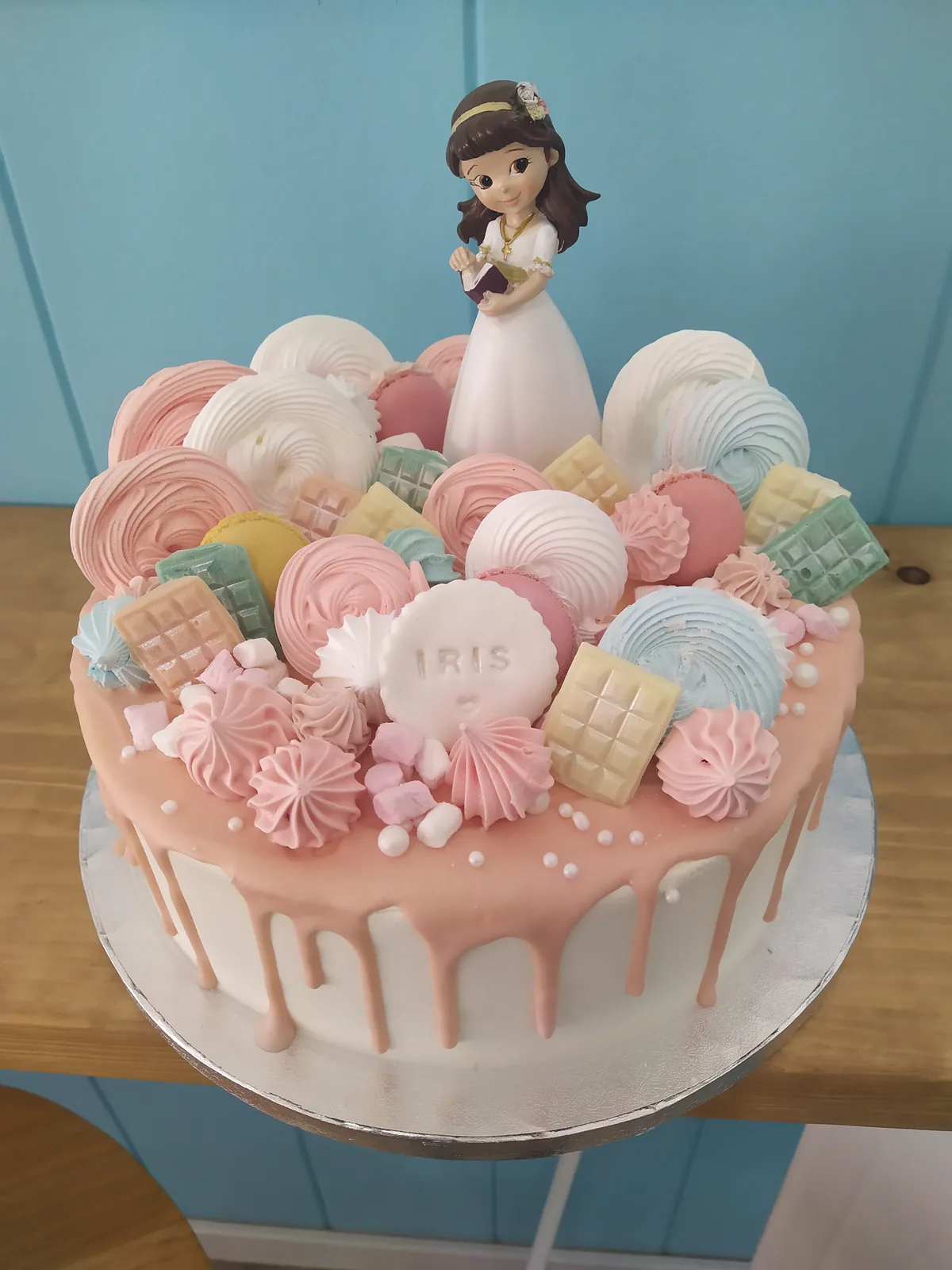 Tarta de comunión de un piso en rosa con drip blanco, merengues y figura de niña