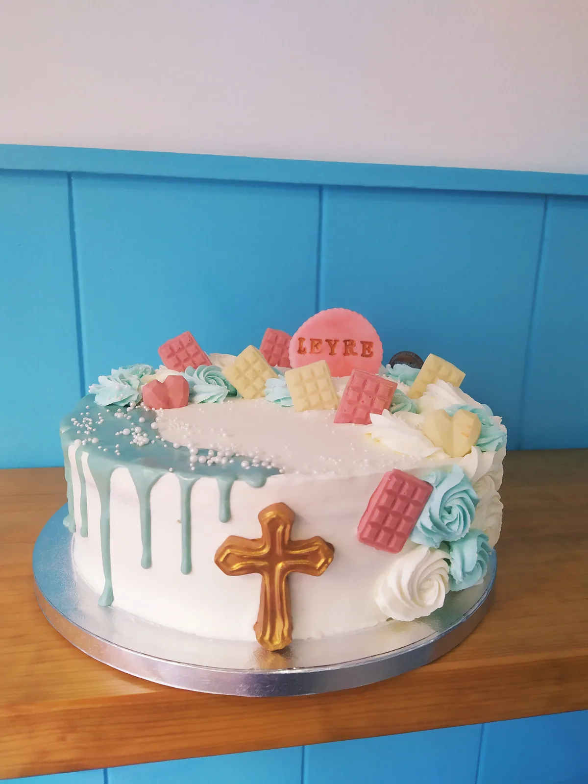 Tarta de comunión blanca con cruz de madera, flores naturales y drip