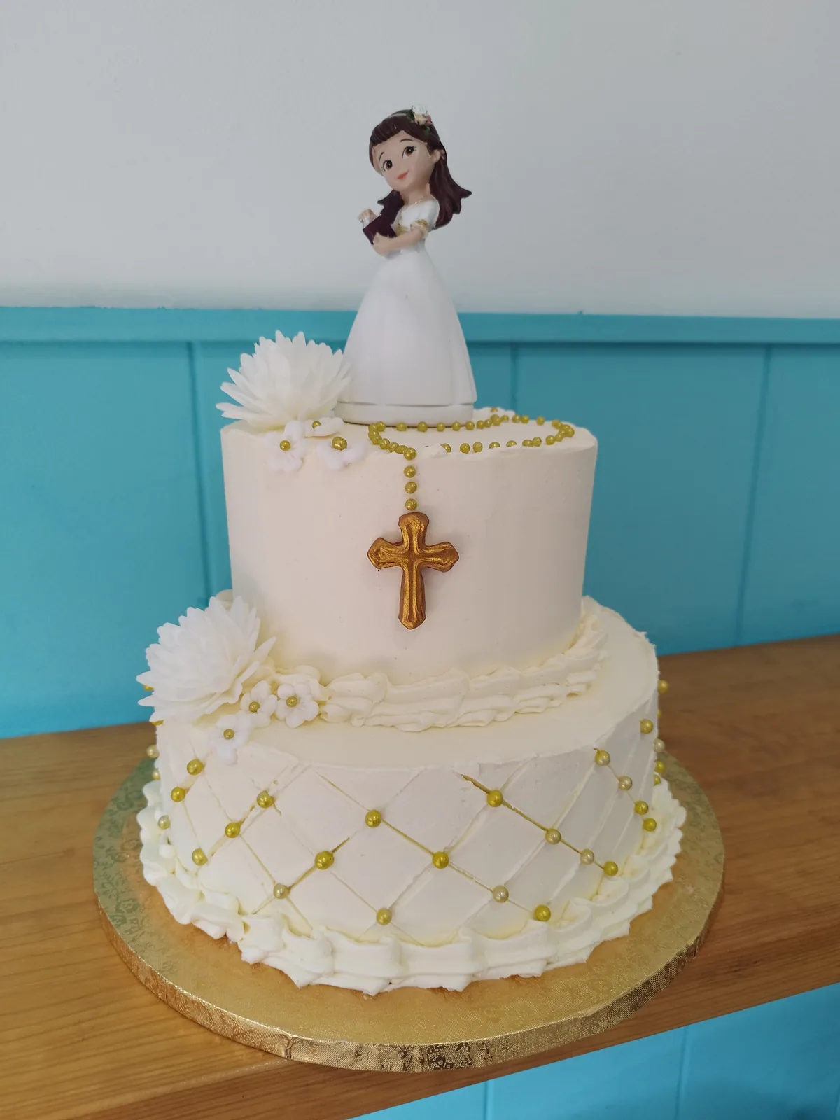Tarta de comunión de dos pisos en blanco y dorado con cruz y figura de niña