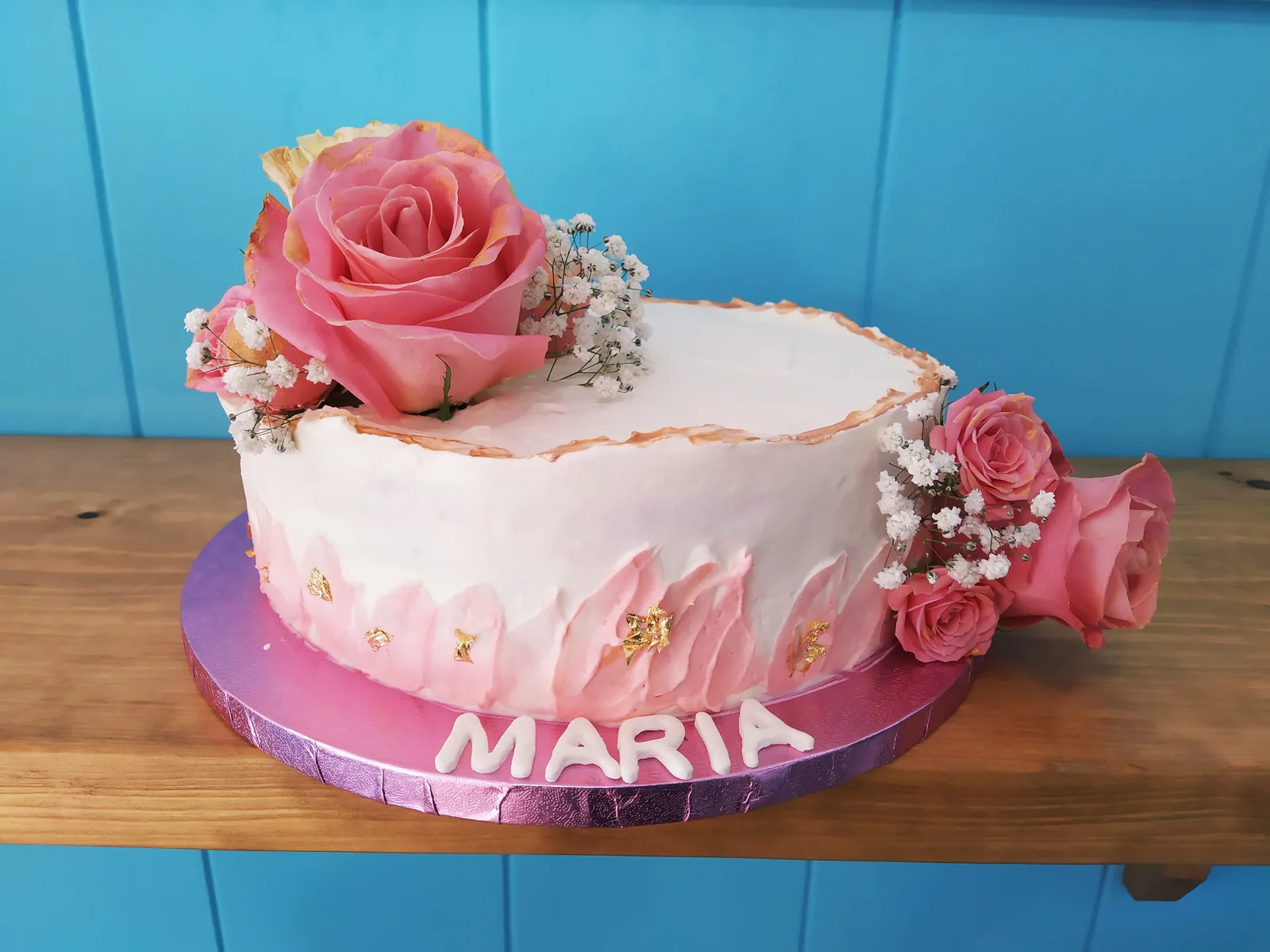 Tarta blanca con rosas naturales rosas y follaje en la parte superior