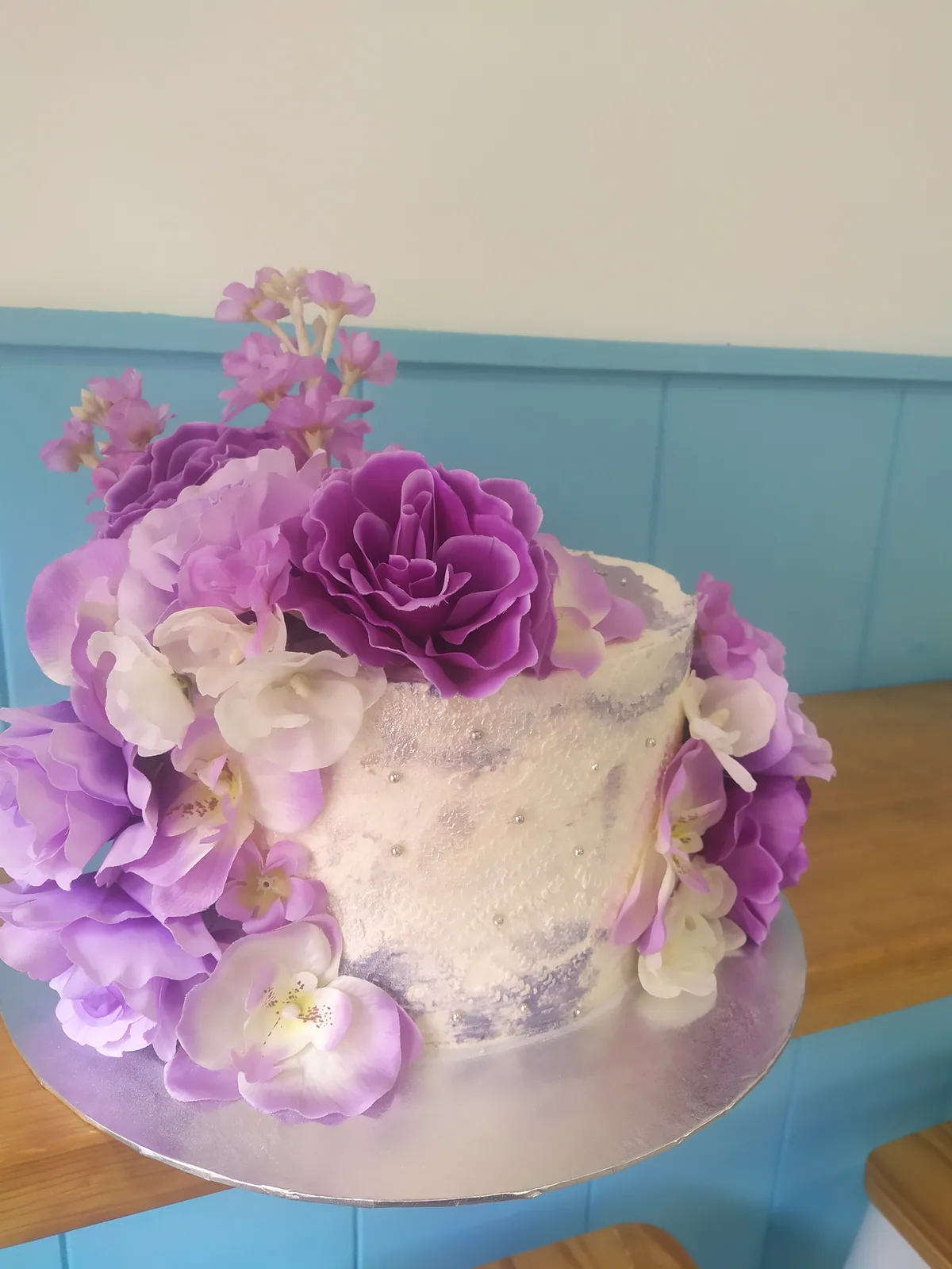 Tarta con flores naturales moradas y lilas sobre cobertura blanca