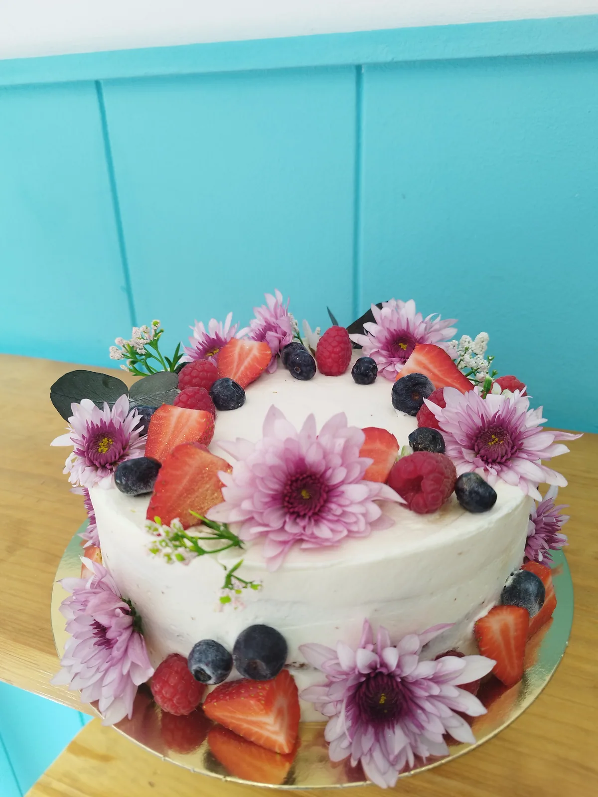 Tarta con flores naturales, fresas y frutos rojos en la parte superior