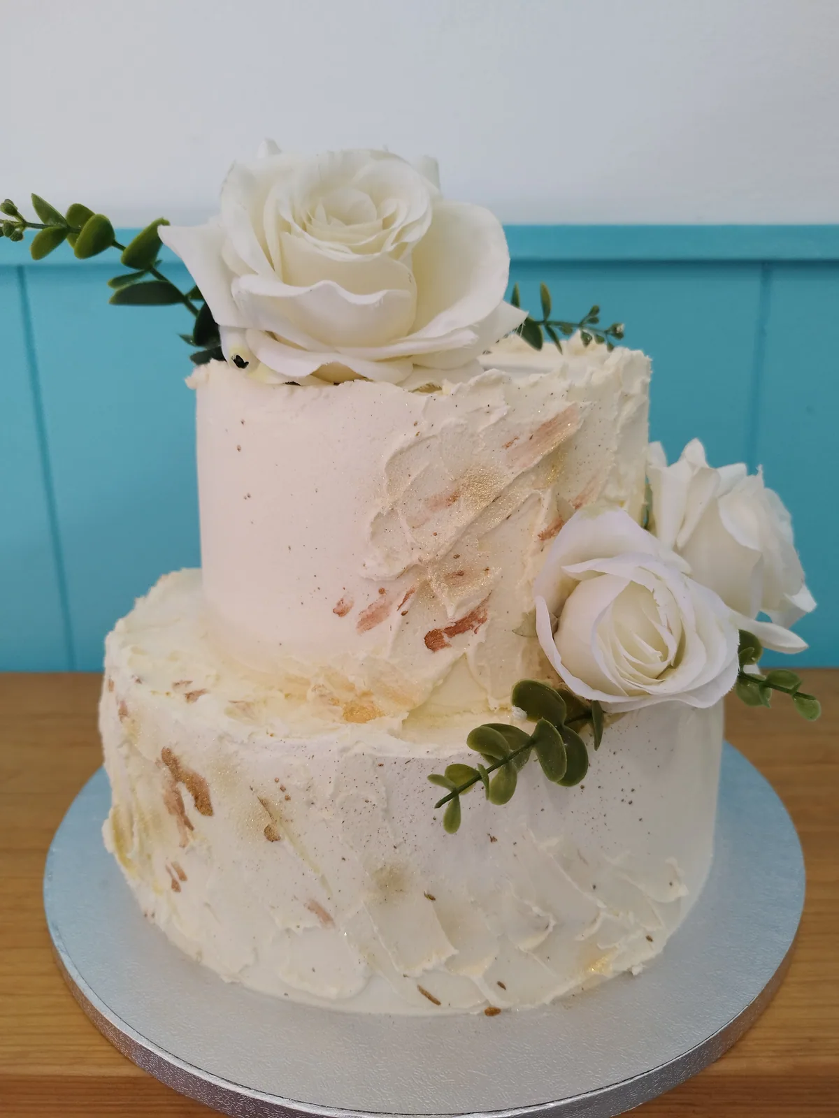 Tarta de dos pisos en blanco con rosas y follaje natural