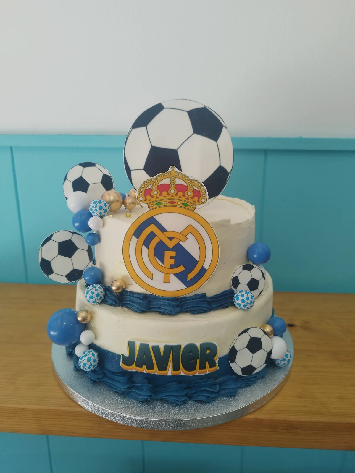 Tarta del Real Madrid de dos pisos con balones, escudo dorado y el nombre Javier