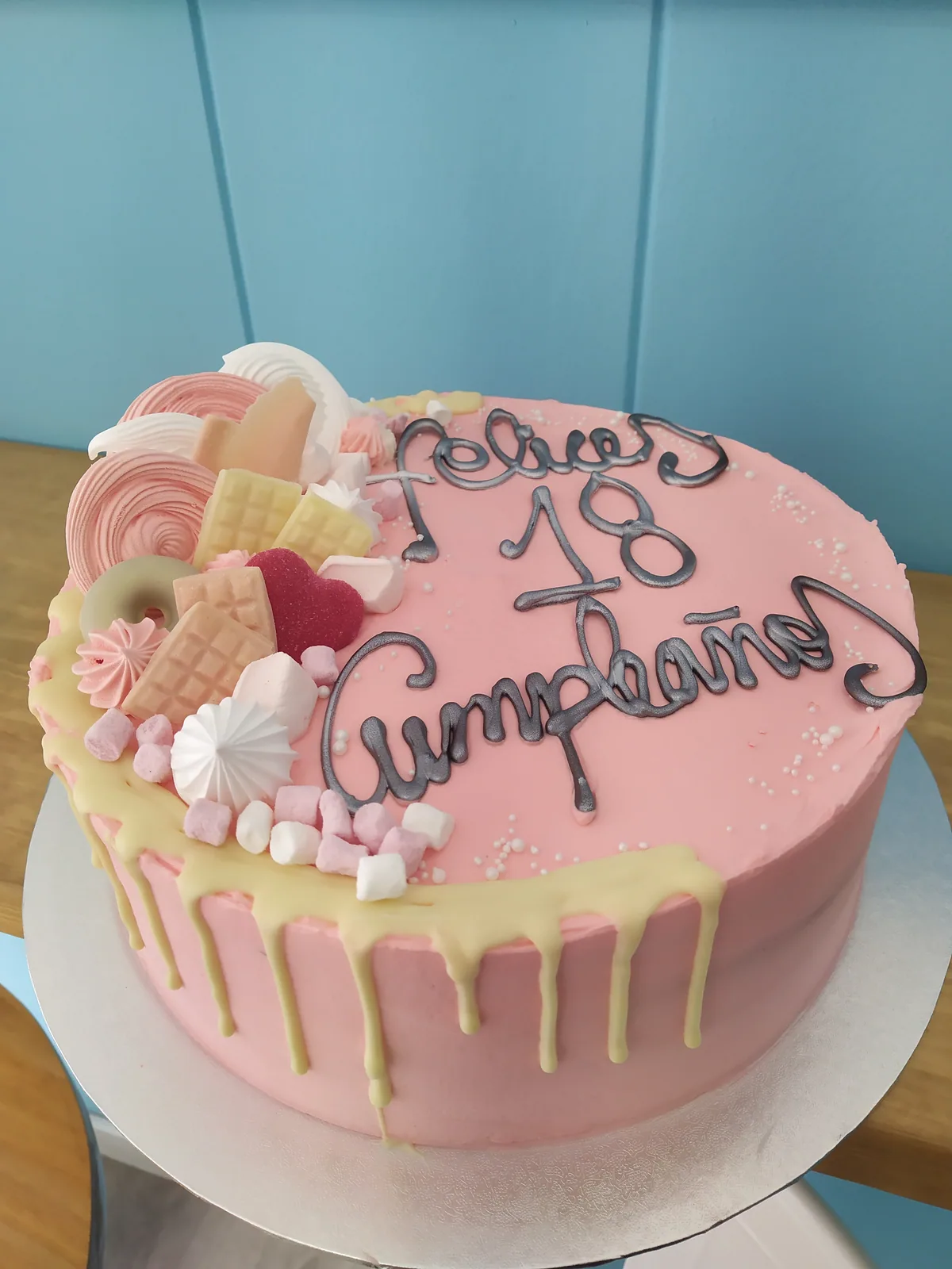Tarta rosa con drip blanco, macarons y frutas en un lateral