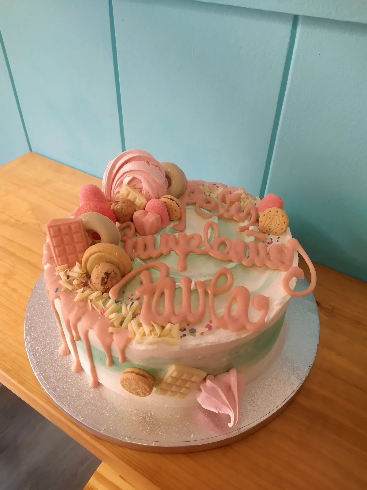 Tarta en tonos rosa con macarons, galletas y felicitación escrita a mano